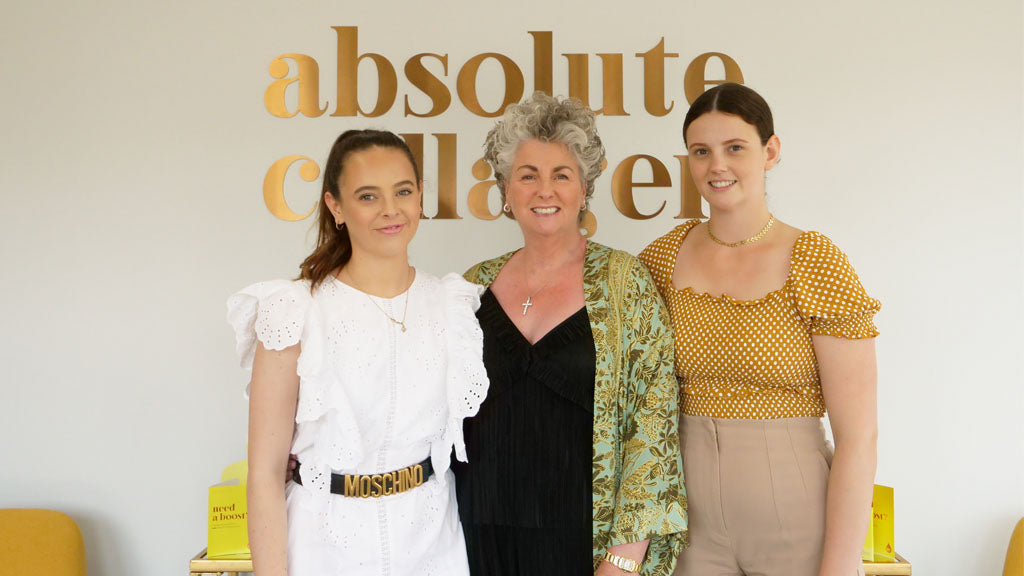 Foto zeigt Maxine, Margot und Darcy Laceby die vor einem Kupfer Absolute Collagen Schild stehen und lächeln